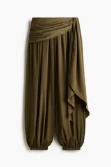 Pantalón globo de tiro alto color verde militar en tejido satinado con leve brillo. Presenta cintura elástica revestida, sección cruzada que se ata en un lateral con caída fluida y bajos elásticos ajustados.