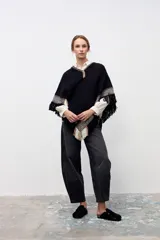 Poncho artesanal de lana en color negro, con diseño de guardas geométricas en tonos beige y blanco en los bordes y flecos decorativos en todo el contorno.