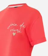 Remera roja de algodón con mangas cortas y cuello redondo. Presenta un bordado con la frase "joie de vivre" y un corazón de strass en el pecho.