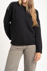 Sweater de lana color negro, de corte oversize, con cuello redondo, mangas largas y detalle de apliques metálicos en los hombros.
