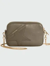 Cartera tipo crossbody de cuero color gris topo, con diseño de estrella pespunteada en el frente y logo de la marca grabado en dorado. Incluye correa de cadena metálica dorada desmontable y cierre superior.