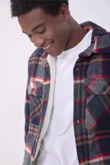 Sobrecamisa de corte holgado con diseño a cuadros en tonos beige y marrón, confeccionada en tejido de textura suave. Presenta cuello clásico, cierre frontal con botones, dos bolsillos con solapa en el pecho y puños abotonados.