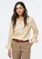 Camisa de corte clásico con cuello camisero, manga larga con puños vueltos y cierre frontal de botones. Presenta un diseño de rayas verticales finas en tono beige.