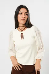 Blusa color manteca de cuello redondo y mangas largas abullonadas con puños elásticos.