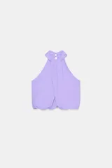 Top corto de cuello halter con diseño delantero cruzado y bajo abullonado con elástico. Presenta un estampado sutil de lunares y cierre en la espalda con botones ocultos.