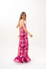 Vestido largo fucsia con estampado abstracto en tonos rosados y morados, cuello halter cruzado y flecos largos en el dobladillo inferior.