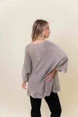 Buzo de tejido liviano con brillo sutil tipo lurex, color beige o dorado claro. Presenta un calce suelto (oversize) con mangas amplias y cuello redondo. El ruedo tiene un detalle de terminación festoneado con pequeños calados.