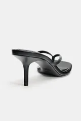 Sandalia de tacón en piel color negro, con diseño tipo thong con tira delantera para el dedo, tacón alto fino y puntera cuadrada.