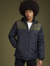 Campera acolchada con capucha, diseño bicolor en azul marino y verde oliva. Presenta cierre frontal, bolsillos laterales y logo estampado en el pecho.