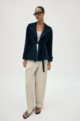 Chaqueta estilo trench corta color azul marino confeccionada con lino. Cuenta con cuello solapa, manga larga con trabilla, bolsillos delanteros de vivo y cierre frontal con lazada ajustable en la cintura.