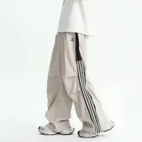 Pantalón deportivo negro de corte muy ancho (baggy) con cierre completo impermeable en los laterales. Presenta tres franjas blancas verticales en el lateral exterior de cada pierna. Posee reguladores en tobillos y cintura.
