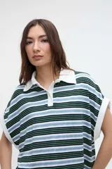 Musculosa tipo polo a rayas horizontales en tonos verdes, azules y blancos, con cuello y ribetes en contraste. Presenta media cartera de botones y tajos laterales en el dobladillo.