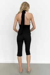 Top negro de cuello halter con escote en pico pronunciado. Presenta un cuerpo estructurado y una parte superior de tul plisado con detalle de lazada tipo foulard en el cuello. Incluye cierre lateral con cremallera oculta.