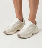 Championes deportivos de material sintético color beige y blanco, con recortes superpuestos, entresuela robusta y suela tractorada.