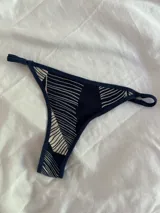 Bombacha de bikini tipo colaless con estampado geométrico de líneas blancas sobre fondo azul marino. Presenta textura acanalada y tiras laterales ajustables.