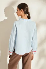 Blusa de lino color marrón con escote en V, cuello con volados y mangas largas con puños fruncidos que presentan detalles en color crudo, al igual que en los hombros. Cuenta con cierre frontal de botones.