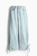 Jean tobillero de denim rígido, tiro alto y diseño curvo de cinco bolsillos con tiras finas para anudar en los bajos.