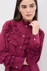 Camisa de manga larga en color rosado, con diseño de volados en cascada en el frente y en los puños. Presenta cuello alto con terminación suave y cierre frontal con botones.