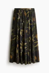 Pollera larga de corte holgado, color negro, con estampado tropical de hojas y flores en tonos verdes y ocres. Presenta tiro alto, cintura elastizada en la espalda con frunces y diseño fluido.