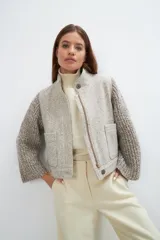 Campera de lana fina color crema, con cuerpo estructurado y mangas de tejido de punto acanalado. Presenta cuello alto, cierre frontal con botones y bolsillos laterales con doble abertura.