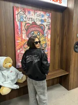 Campera de cuero sintético negro con diseño tipo bomber, cuello camisero y puños y ruedo elásticos. Presenta un bordado grande en la espalda con tipografía cursiva en color blanco.