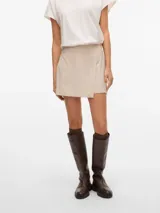 Pollera short de tiro alto y fit holgado, de color beige, con diseño cruzado en el frente y cierre lateral invisible.