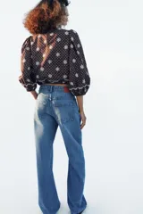 Blusa azul marino con estampado de lunares blancos, cuello redondo y mangas abullonadas. Presenta detalles de bordados perforados, volantes delanteros y acabados elásticos.