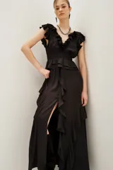 Vestido largo negro con escote en V y volados en el borde del escote y mangas. Presenta un corte peplum con elástico en la cintura y falda larga con abertura frontal y volados.
