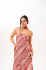Vestido largo de crochet con escote strapless y lazo integrado para el cuello, con diseño de patrón en zigzag en tonos rojos, blancos y beige, y aberturas laterales en la falda.
