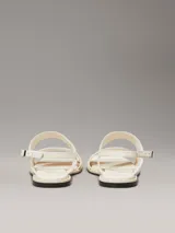 Sandalias planas blancas de cuero sintético, con puntera cuadrada y dos tiras anchas. La tira superior tiene el logo de Calvin Klein grabado.