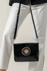 Sobre de mano color bordó en cuero charolado, con solapa frontal decorada con una piedra ágata natural engarzada. Incluye correa larga extraíble y cierre trasero.