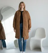 Camperón largo de diseño acolchado con patrón de rombos, color camel. Presenta cuello redondo tipo bomber, cierre frontal completo y puños tejidos acanalados en tono a juego.