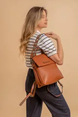 Mochila tipo cartera con tapa, confeccionada en símil cuero color suela. Cuenta con doble compartimento, división interna, cierre de seguridad y bolsillo trasero con cierre. Incluye una correa frontal decorativa con tachas metálicas.