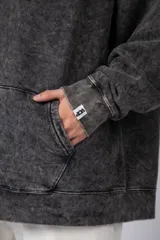 Buzo canguro oversize de algodón friza con efecto de teñido artesanal acid wash en color gris oscuro. Presenta capucha con cordones ajustables, bolsillo frontal tipo canguro y estampa pequeña en el pecho.
