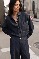 Jeans de tiro alto color azul oscuro, con cintura elástica en la espalda, bolsillos delanteros y bolsillos de plastrón en la espalda. Presenta pernera ancha y cierre frontal con cremallera y botón a presión.