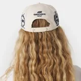 Gorra color beige con visera plana y parche bordado en el frente con escudo y la inscripción 'GOLF'.