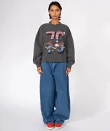 Buzo de algodón color marrón, con cuello redondo y mangas largas abullonadas con puños ajustados. Presenta un estampado grande con el número "76", un águila americana y texto. El borde inferior es cortado y deshilachado.