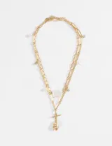 Collar dorado de acero con doble cadena, una de eslabones rectangulares y otra de eslabones más pequeños. Tiene dijes colgantes de perlas y strass.
