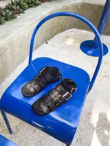 Sandalias negras de cuero vacuno con plataforma baja y tiras anchas. Presentan hebillas plateadas ajustables y pulsera superior desmontable.