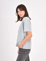 Remera de algodón color gris claro con efecto lavado, cuello redondo y detalle de pequeñas tachas metálicas dispersas en la parte superior delantera y mangas.