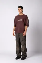 Remera de tejido de punto con textura calada, color crema con rayas verticales sutiles. Presenta cuello en V, mangas cortas con franjas laterales en color marrón oscuro y logo bordado en el centro del pecho.