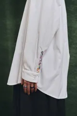 Camisa de corte oversize con mangas largas y puños abotonados. Presenta un diseño bicolor con cuerpo blanco y un canesú delantero con estampado floral multicolor.