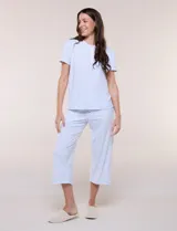 Pijama de dos piezas con estampado floral en tonos azules sobre fondo blanco, compuesto por una remera de manga corta con cuello redondo y botones frontales, y un pantalón capri con cintura elastizada y bolsillos.