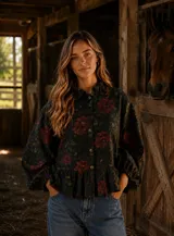 Camisa de lino con estampado floral oscuro, cuello con volados, cierre frontal de botones y mangas largas abullonadas con puños elásticos. Presenta un diseño con volado en el ruedo.