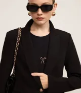 Blazer de sastrería en crepé color negro, con cuello solapa, cierre frontal de un solo botón dorado y bolsillos laterales con solapa.