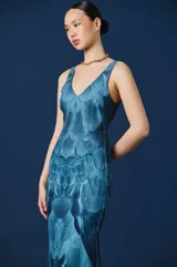Vestido largo de corte sirena con escote en V y breteles anchos. Presenta un estampado integral que simula texturas de plumas en tonos azules degradados.