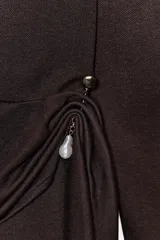 Vestido largo de color marrón oscuro, con cuello fluido tipo bote, manga larga y detalle de fruncido lateral con broche metálico en la cintura.