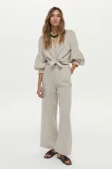 Camisa de lino color beige, con escote en V, cuello mao y mangas abullonadas tres cuartos. Cuenta con cierre frontal de botones y tiras ajustables para atar en la cintura.