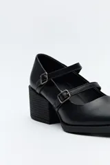 Zueco estilo Mary Jane color negro charol, con doble tira y hebillas metálicas. Presenta punta cuadrada y taco ancho de altura media.