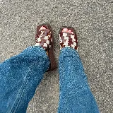 Zueco de mujer con plataforma y taco bajo, color marrón oscuro. La capellada es de tiras trenzadas en patrón damero (cuadros) en tonos marrón oscuro y blanco/beige.